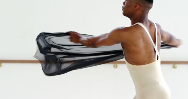 Male ballet dancer practicing in studio, creating fluid motion with black fabric. Useful for dance training materials, fitness and exercise promotions.