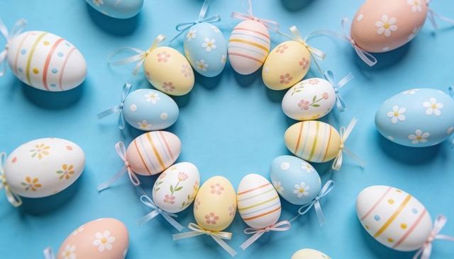 Hand-painted pastel Easter wreath with ribbon-decorated eggs on soft blue backdrop