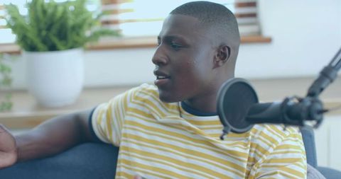 Young man recording podcast on couch with professional microphone and natural daylight