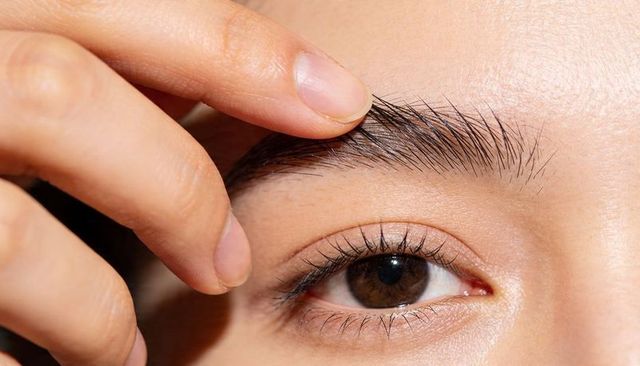 Finger parting eyebrow closeup showing brown eye, long lashes and skin texture, macro lighting
