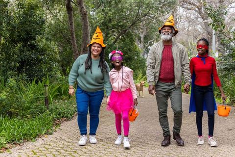 African american family walking park trick-or-treating with pumpkin hats and colorful costumes