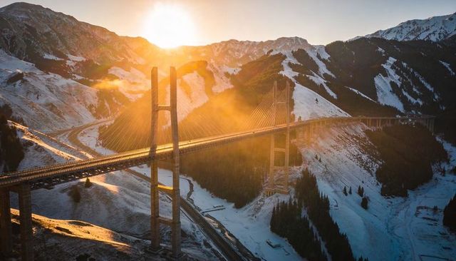 Sunrise light flooding cable-stayed viaduct over snow-covered alpine valley