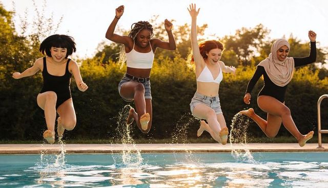 Jumping friends splashing at backyard pool during golden hour, diverse women celebrating