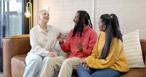Laughing diverse friends chatting and bonding on cozy brown leather sofa in living room