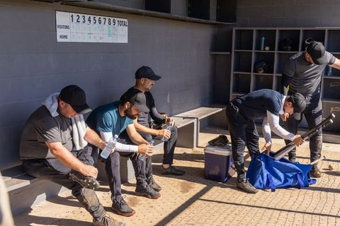 Baseball teammates packing gear and hydrating in dugout before amateur game on sunny day