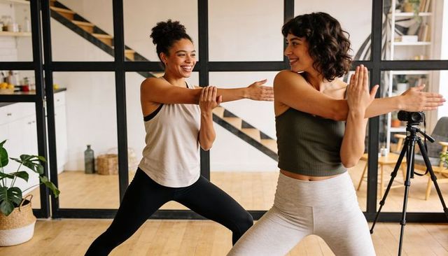 Two women stretching in bright home studio recording workout session for online class