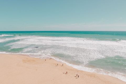Sunlit turquoise waves rolling toward wide sandy beach with distant walkers