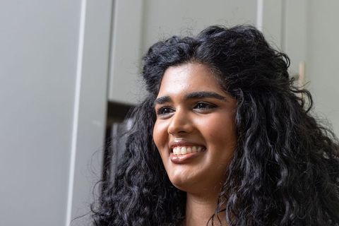 Confident indian woman smiling and gazing away at home with curly hair and warm makeup