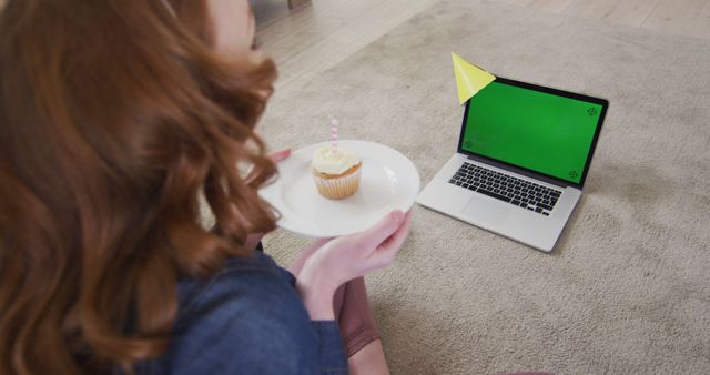 Happy caucasian woman with birthday cake having laptop video call with copy space. Domestic life, celebration, technology and lifestyle, unaltered.