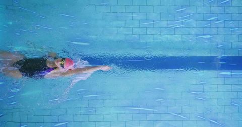 Professional swimmer gliding in pool with pink cap and tinted goggles