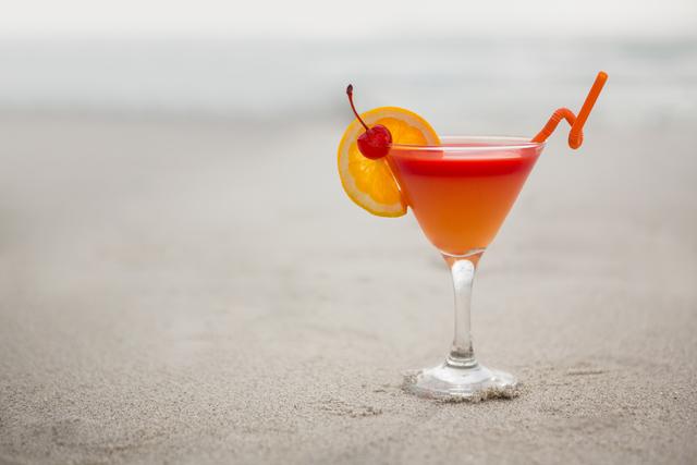 Refreshing cocktail with orange slice and cherry on sandy beach. Ideal for travel brochures, summer vacation promotions, beach resort advertisements, and social media posts about relaxation and leisure.