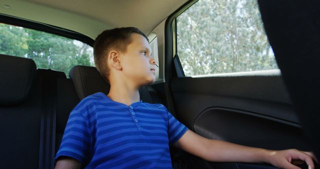 Young boy in the backseat of a car, looking out the window. Has a thoughtful expression, dressed in a blue-striped shirt. Scene highlights themes of travel, adventure, and childhood. Ideal for use in travel-related content, road trip campaigns, and family-oriented advertisements.