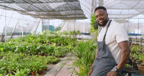 Smiling gardener in nursery greenhouse with variety of plants