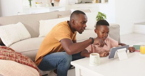 Father guiding son using tablet for learning and play in bright living room