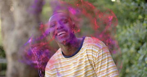 Laughing man enjoying vibrant magenta and purple powder burst in garden celebration