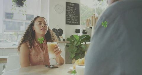 Young woman sipping iced latte at sunlit cafe table holding smartphone and croissant