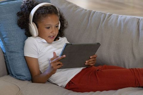 Child relaxing on couch using tablet with headphones for learning and screen time at home