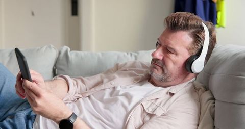 Mature Man Relaxing at Home Reading on Tablet with Headphones