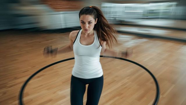Young woman jumping rope for cardio workout on hardwood floor with mirrored wall