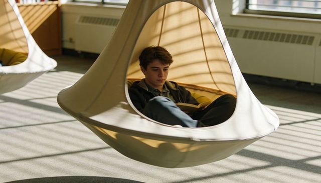 Teenager reading in suspended pod chair with sunlit stripes and cozy nook