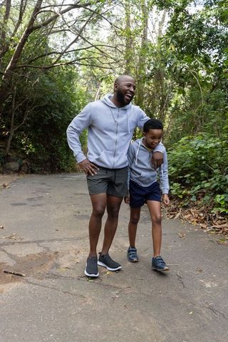 African american father and son walking laughing on wooded trail wearing gray hoodies