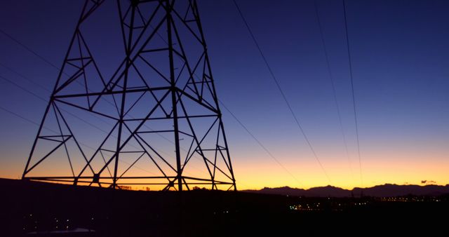 Electric tower silhouetted against a vibrant sunset sky. Ideal for topics on energy infrastructure, evening landscapes, electricity and utilities. Use for presentations, articles or websites discussing power supply, renewable energy, or scenic views of industrial structures.