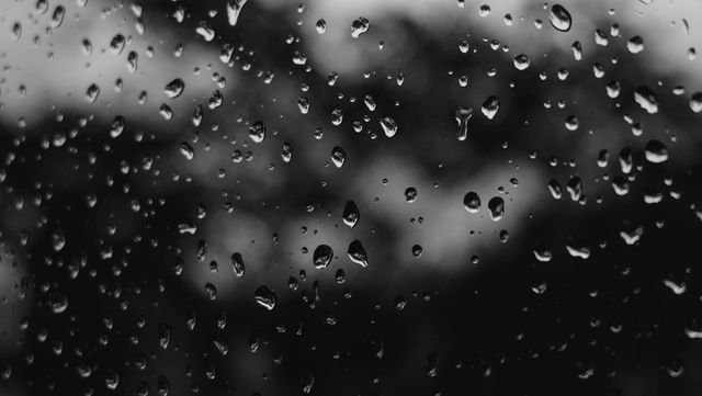 Close-up of raindrops on window glass creating a sense of a rainy or overcast day. Perfect for use in weather-related articles, backdrops for digital art, representing emotions like melancholy or reflection, and enhancing the aesthetic of presentations and creative works needing a natural rain backdrop.