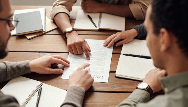 Business team reviewing contract together around wooden table pointing discussing details