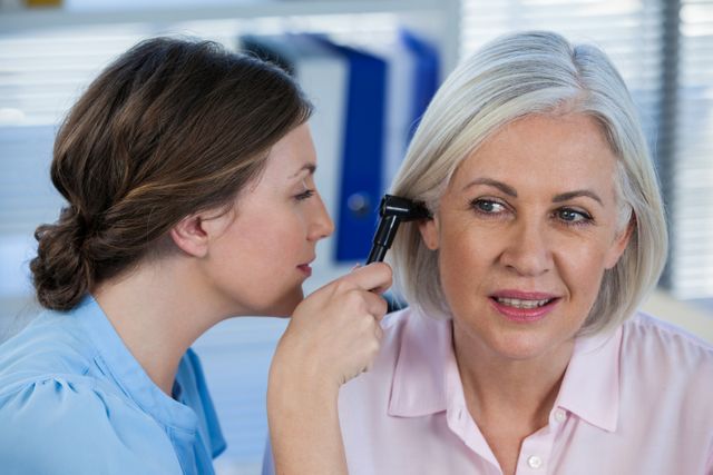 Doctor examining patients ear with otoscope in clinic