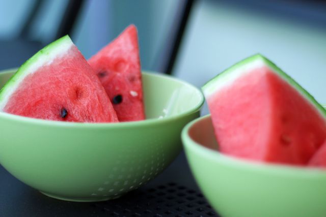 Close-up view of fresh watermelon slices arranged in green bowls. Ideal for content about healthy eating, summer fruits, and refreshing snacks. Suitable for use in food blogs, summer event promotions, and vegan lifestyle articles.