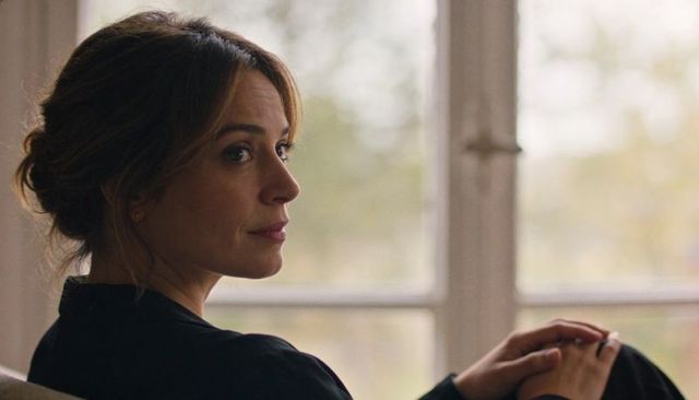 Woman gazing out multi-pane window, clasping hands on armrest, contemplative daylight portrait