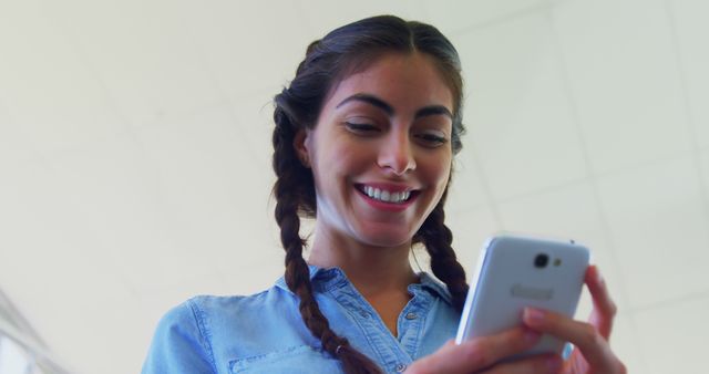 A young woman is smiling as she looks at her smartphone, with copy space. Her cheerful expression suggests she may have received good news or is enjoying a conversation.