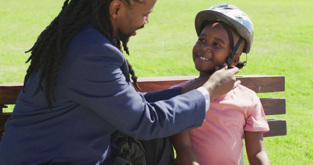 Father securing helmet on son's head in park, focusing on safety and good parenting practice. Great for content about family bonds, outdoor activities, child safety, loving parenting moments, and father-son relationships.