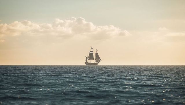 Vintage sailing ship on open ocean at sunset
