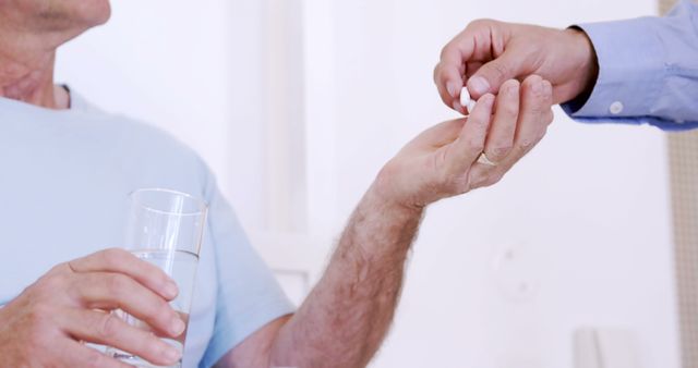 A medical professional is giving a pill to an elderly patient who is holding a glass of water. Ideal for use in articles about elderly care, healthcare, medication management, medical assistance, and clinical nursing scenarios.