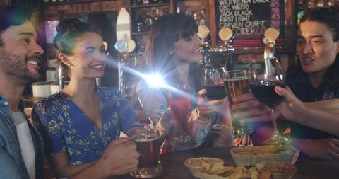 Friends toasting drinks at lively pub bar counter with beer, wine, cocktails