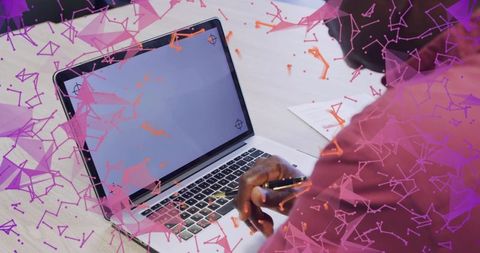 Senior man typing on laptop holding pen in maroon shirt with purple geometric overlay
