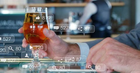 Businessman holding craft beer and tapping smartphone with social media icons at bar