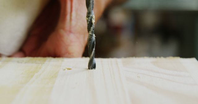 Focus on a drill drilling a whole in a wood plank in workshop