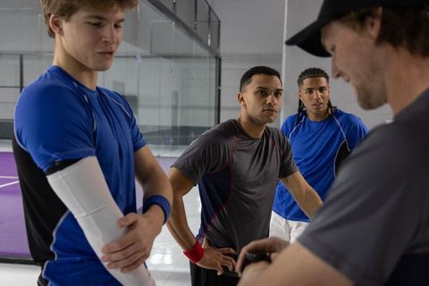 Multicultural male athletes listening to coach checking watch during indoor court training