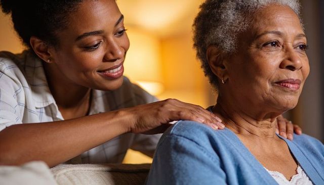 Adult daughter comforting senior mother with gentle shoulder massage on cozy sofa