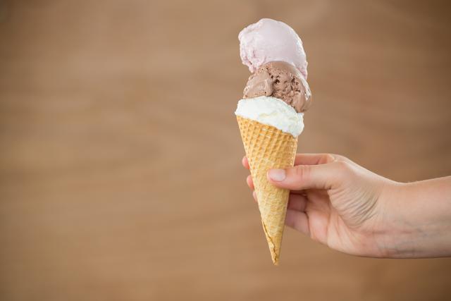 Close-up of hand holding waffle cone with three different scoops of ice cream