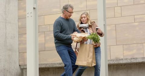 Senior couple descending urban steps carrying grocery bag with greens and takeaway coffee