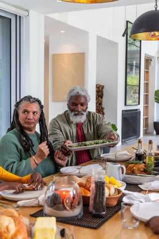Senior couple passing green salad platter at cozy family dinner with candlelight ambience