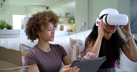 Two African American Friends Trying Virtual Reality While Using Tablet on Sunlit Sofa