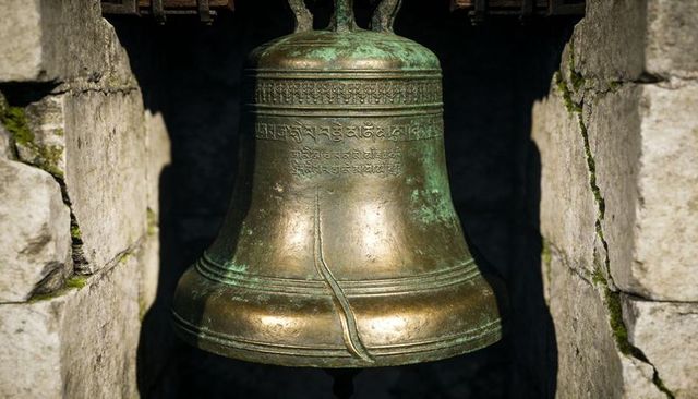 Hanging bronze bell showing verdigris, engraved bands and cracked rim in sunlit stone niche