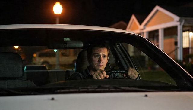 Pensive male driver gripping steering wheel at night on suburban street under lamp moody