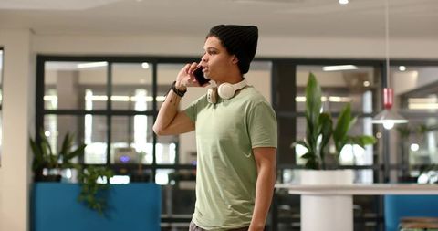 African american man talking on phone wearing beanie and headphones in modern lounge
