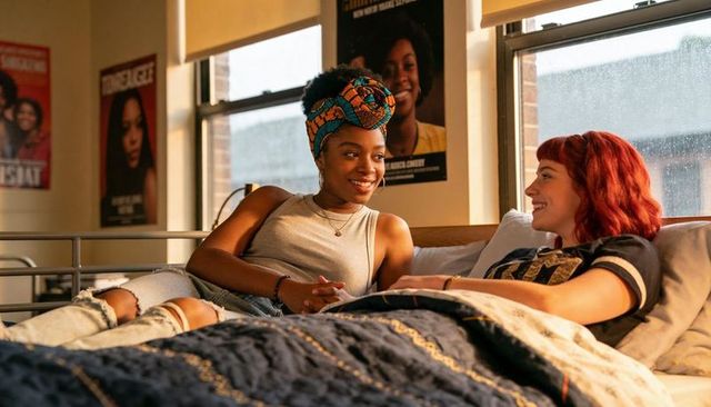 Chatting college friends lounging on dorm bed with headwrap, ripped jeans, sunlight