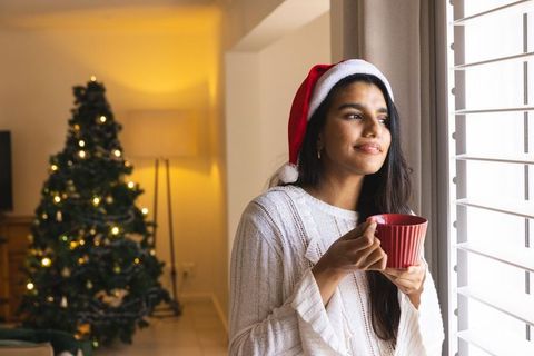 Smiling Woman in Santa Hat with Mug Near Christmas Tree